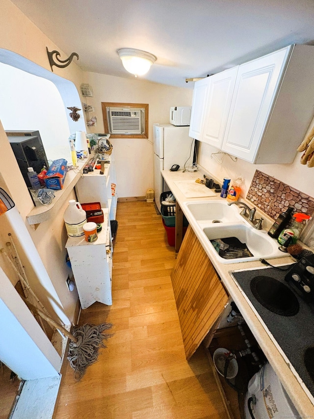 kitchen featuring white appliances, light wood-type flooring, white cabinetry, a sink, and a wall mounted AC