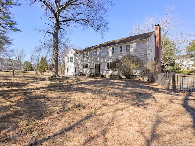 rear view of house with a chimney, fence, and a gate