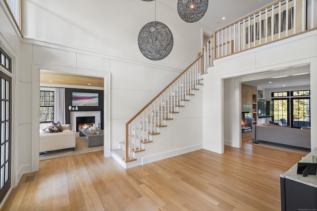 entrance foyer with a wealth of natural light, light wood-type flooring, a lit fireplace, and stairs