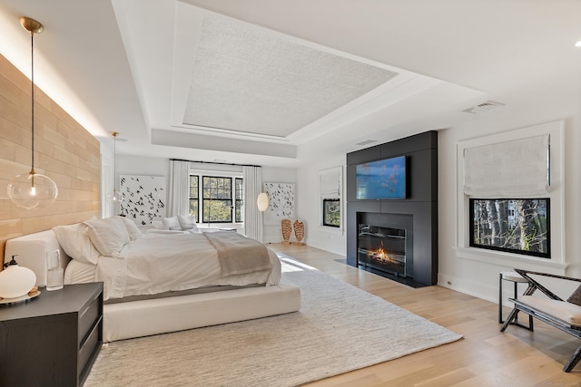 bedroom with light wood-type flooring, baseboards, visible vents, a raised ceiling, and a fireplace with flush hearth