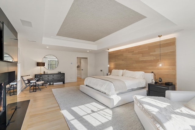 bedroom with light wood finished floors, a tray ceiling, wooden walls, visible vents, and baseboards
