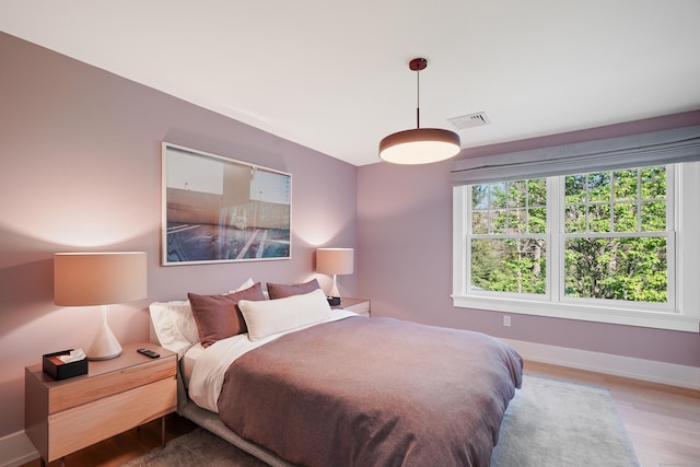 bedroom with baseboards, visible vents, and wood finished floors