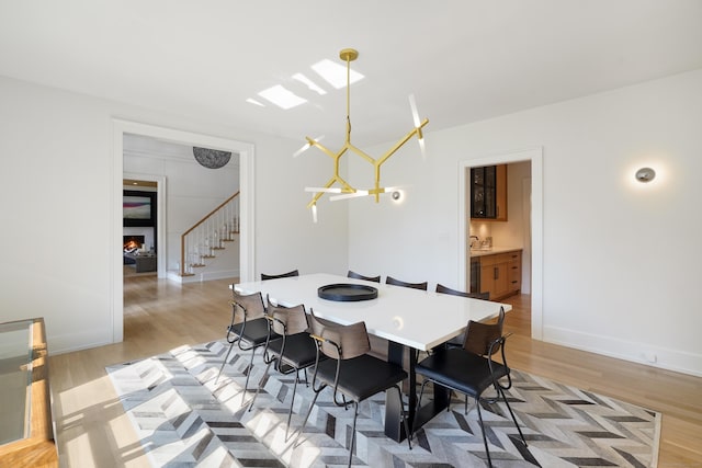 dining space with a warm lit fireplace, stairway, and light wood-type flooring
