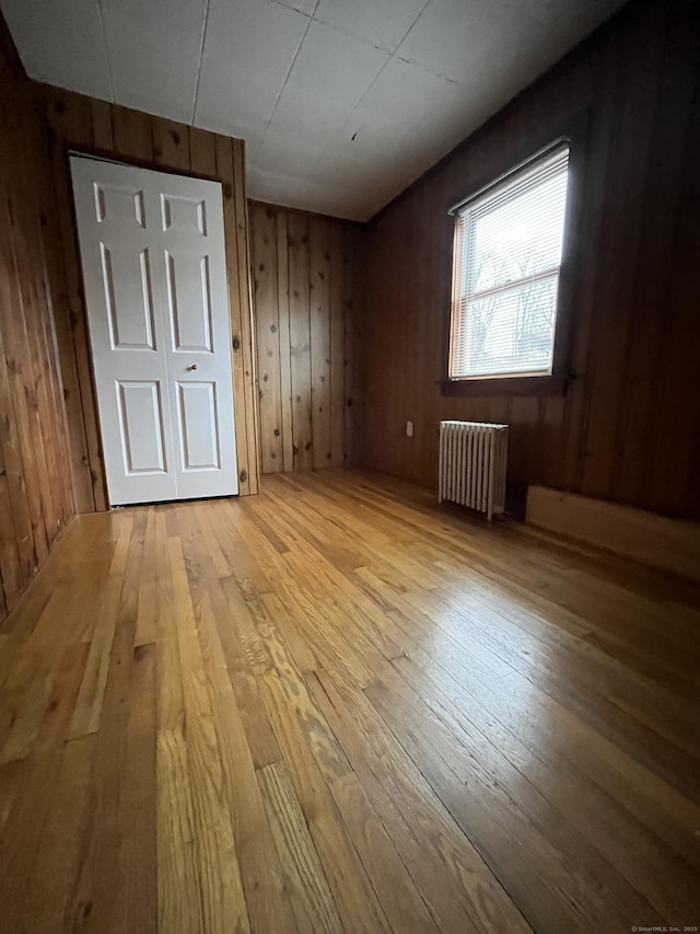 unfurnished room with wood walls, hardwood / wood-style floors, and radiator heating unit