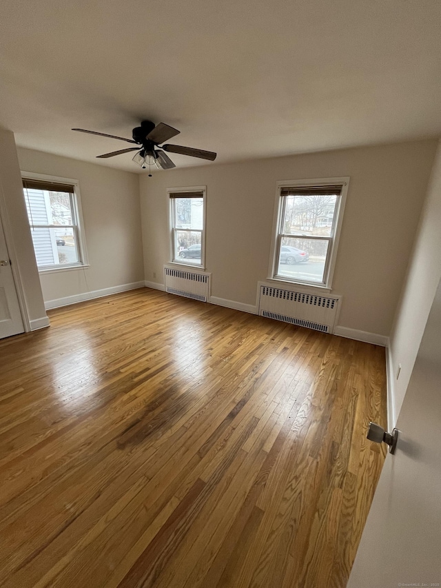 unfurnished room featuring plenty of natural light, radiator heating unit, and wood finished floors