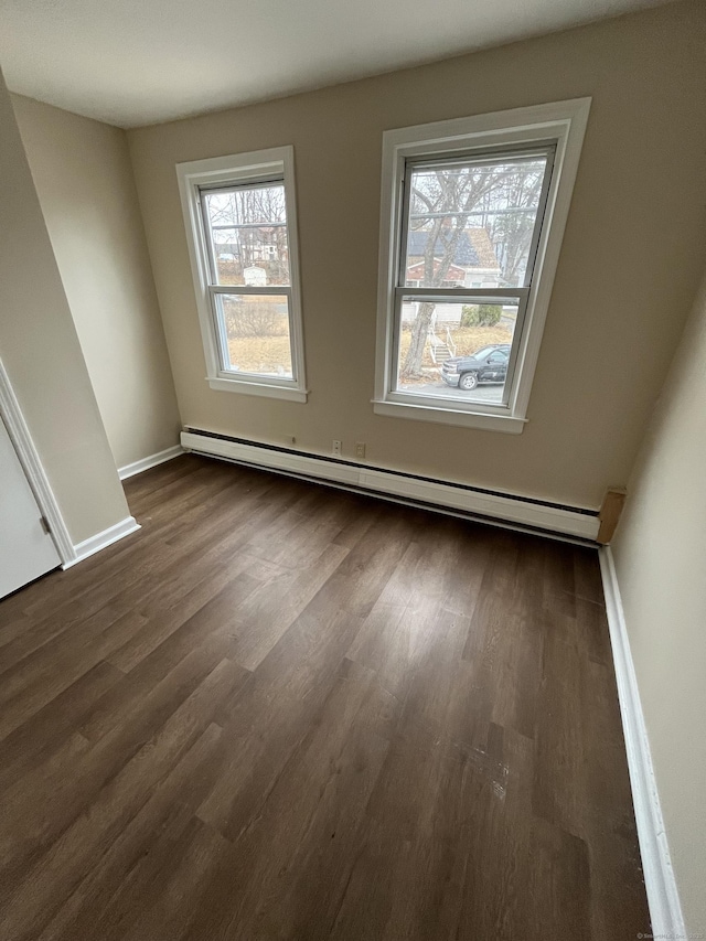 spare room featuring a baseboard heating unit, dark wood-style floors, and baseboards