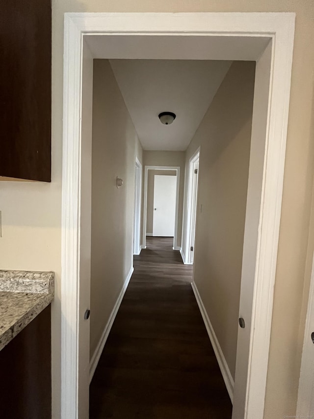 hallway featuring dark wood-style flooring and baseboards