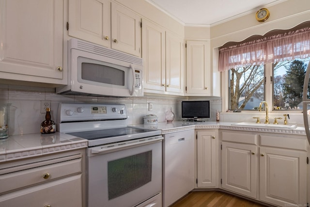 kitchen with white appliances, a sink, white cabinets, crown molding, and tasteful backsplash