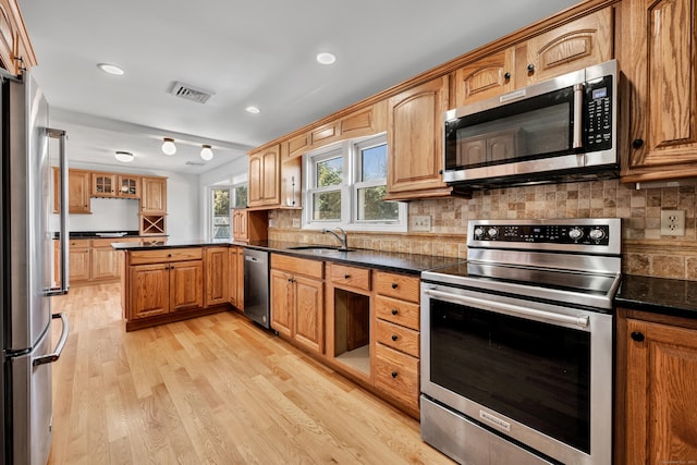 kitchen with dark countertops, visible vents, appliances with stainless steel finishes, a peninsula, and a sink