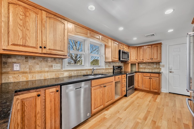 kitchen with visible vents, dark stone countertops, light wood-style flooring, appliances with stainless steel finishes, and a sink