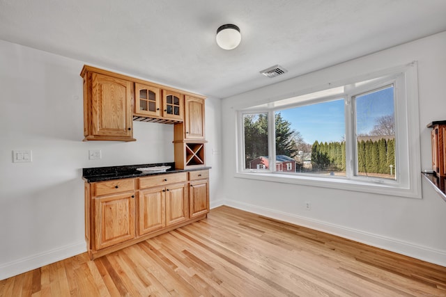 kitchen featuring visible vents, baseboards, glass insert cabinets, and light wood-style floors