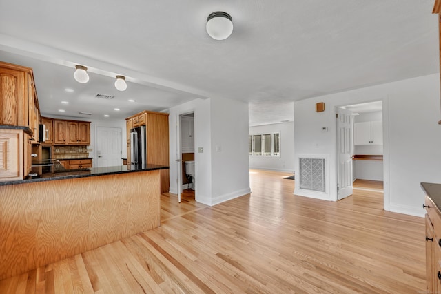 kitchen with dark countertops, refrigerator, a peninsula, and light wood finished floors