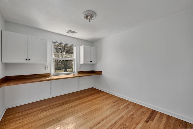 kitchen featuring a breakfast bar area, visible vents, light wood-style flooring, built in desk, and white cabinetry