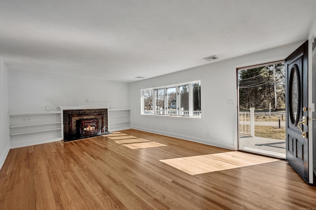 unfurnished living room with visible vents, a brick fireplace, light wood-type flooring, and baseboards