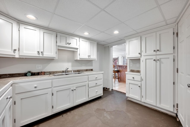 kitchen featuring concrete flooring, light countertops, recessed lighting, white cabinets, and a sink