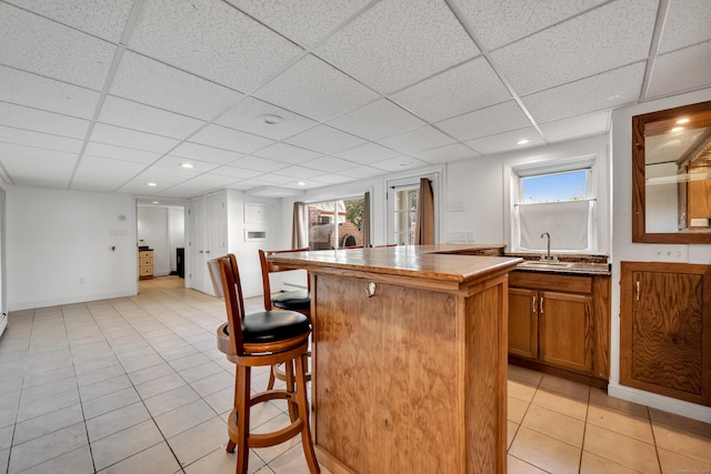 kitchen featuring a kitchen island, a drop ceiling, a breakfast bar area, light tile patterned floors, and brown cabinetry