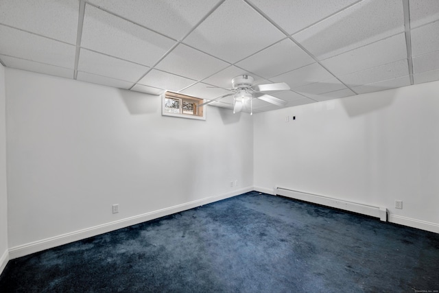 below grade area featuring dark colored carpet, a baseboard heating unit, baseboards, and a paneled ceiling