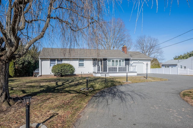 ranch-style home with a front yard, driveway, a porch, an attached garage, and a chimney