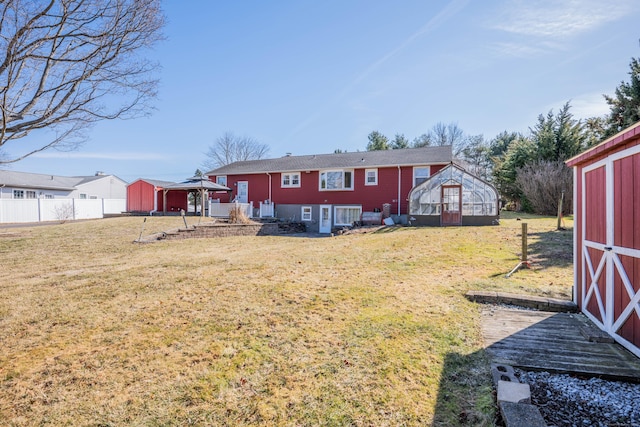 rear view of property with a greenhouse, an outbuilding, a lawn, and fence