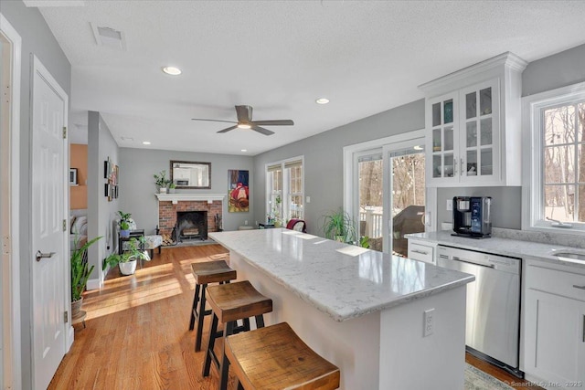 kitchen featuring visible vents, light wood-style floors, white cabinets, stainless steel dishwasher, and a center island