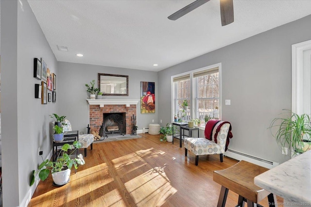 living area featuring visible vents, a baseboard heating unit, a brick fireplace, wood finished floors, and baseboards