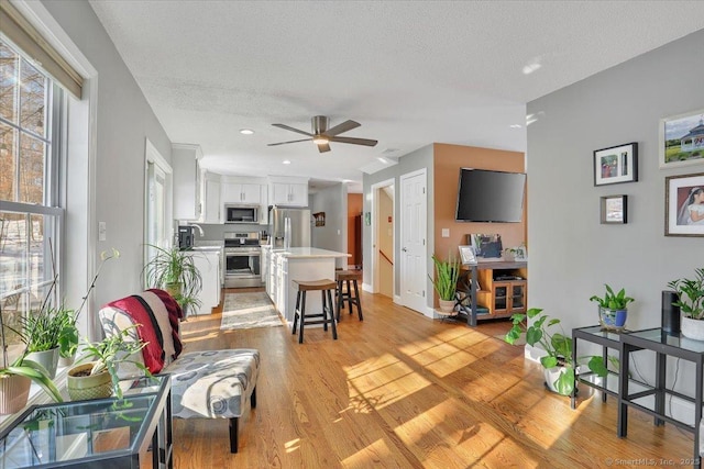 living room featuring light wood-style floors, ceiling fan, baseboards, and a textured ceiling