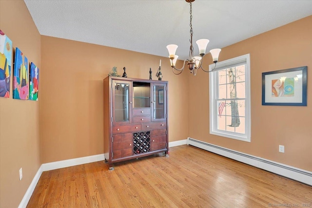 unfurnished dining area with a baseboard radiator, an inviting chandelier, baseboards, and wood finished floors