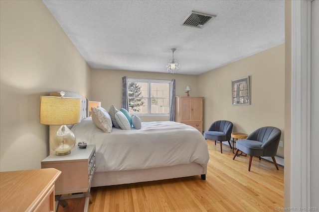 bedroom with a textured ceiling, light wood-type flooring, and visible vents