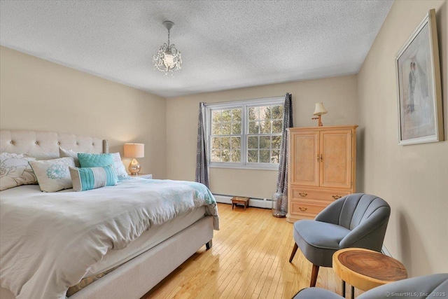 bedroom featuring a baseboard heating unit, light wood-style flooring, and a textured ceiling