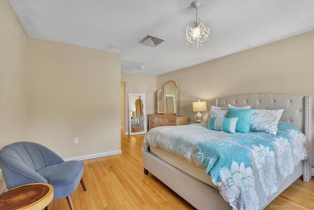 bedroom featuring light wood finished floors, baseboards, visible vents, an inviting chandelier, and a textured ceiling