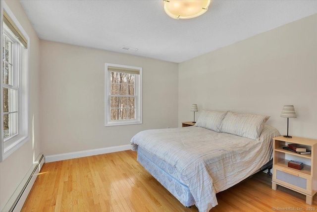 bedroom featuring visible vents, a baseboard heating unit, a textured ceiling, wood finished floors, and baseboards