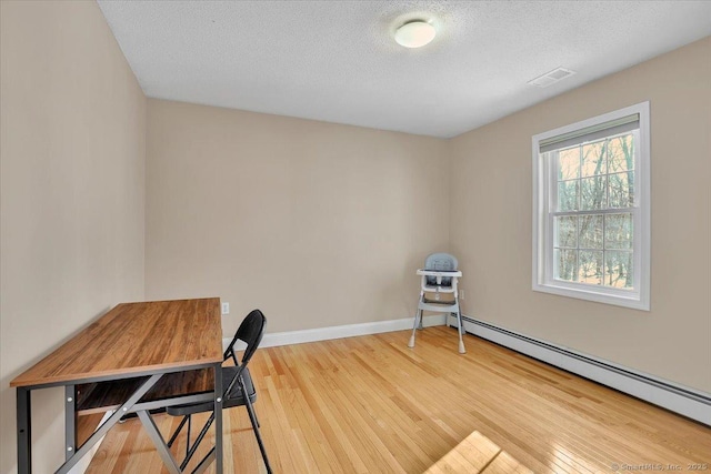 office area with a baseboard radiator, visible vents, a textured ceiling, wood finished floors, and baseboards