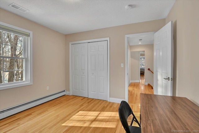 unfurnished office with a baseboard heating unit, visible vents, a textured ceiling, and light wood finished floors