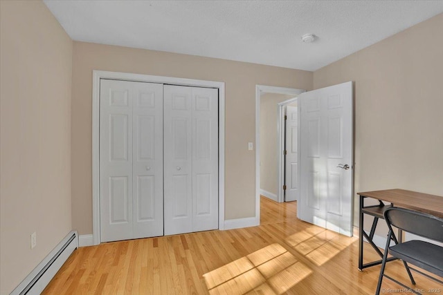 bedroom featuring a baseboard heating unit, light wood finished floors, a closet, and baseboards