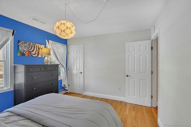 bedroom with a textured ceiling, a baseboard heating unit, wood finished floors, visible vents, and baseboards