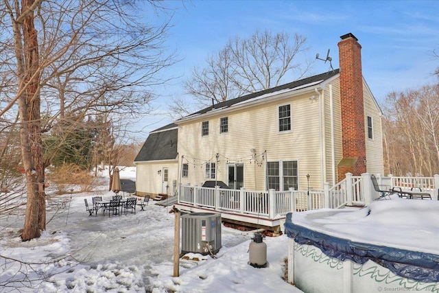 snow covered property featuring a deck, outdoor dining space, a chimney, and central AC unit