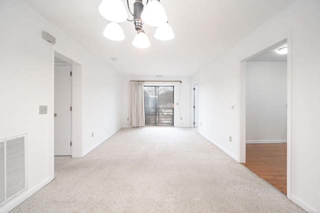 carpeted spare room with an inviting chandelier, baseboards, and visible vents