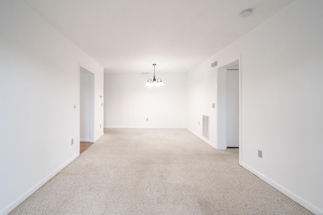 empty room featuring baseboards, visible vents, a chandelier, and light colored carpet