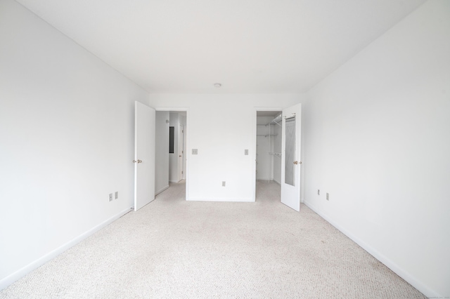 unfurnished bedroom featuring a walk in closet, a closet, light colored carpet, and baseboards