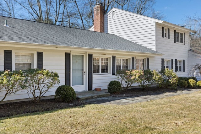 view of front of house featuring a front lawn, a chimney, and a shingled roof