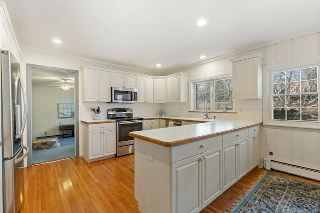 kitchen with stainless steel appliances, light wood-style floors, a peninsula, and a baseboard radiator