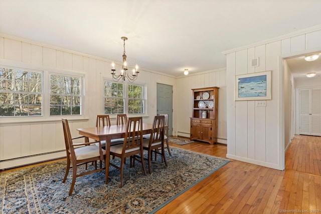 dining area with a chandelier, light wood-style flooring, crown molding, and a baseboard heating unit