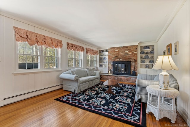 living area with built in shelves, baseboard heating, a brick fireplace, and hardwood / wood-style flooring