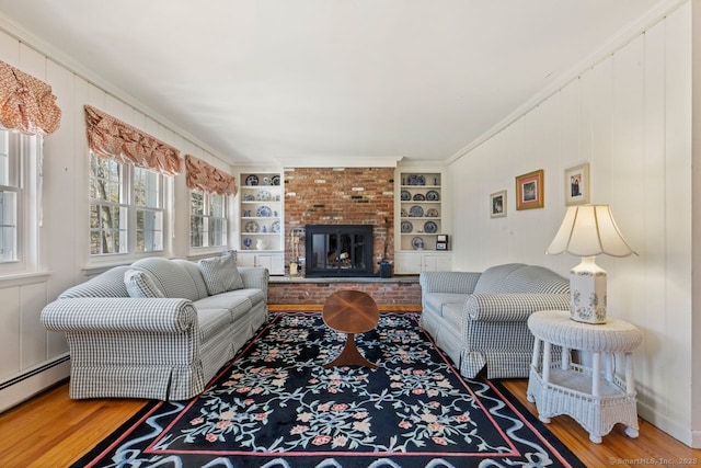 living room featuring built in features, a brick fireplace, wood finished floors, and crown molding