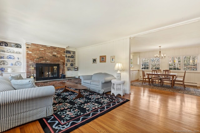 living room with built in shelves, a notable chandelier, wood finished floors, and a fireplace