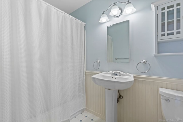 full bath with a wainscoted wall, curtained shower, and toilet