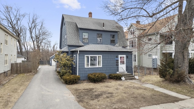 colonial inspired home featuring a shingled roof, an outdoor structure, fence, a gambrel roof, and a chimney