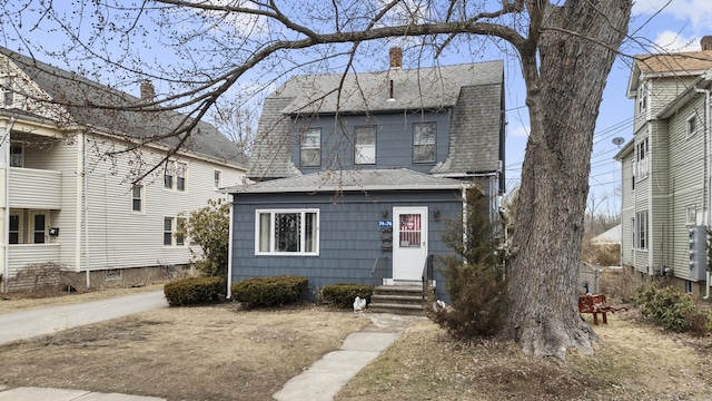 colonial inspired home featuring a shingled roof, entry steps, and a chimney