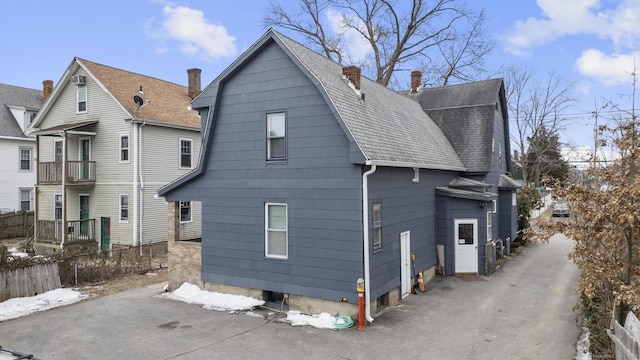 view of side of property featuring driveway, a shingled roof, a gambrel roof, a chimney, and fence