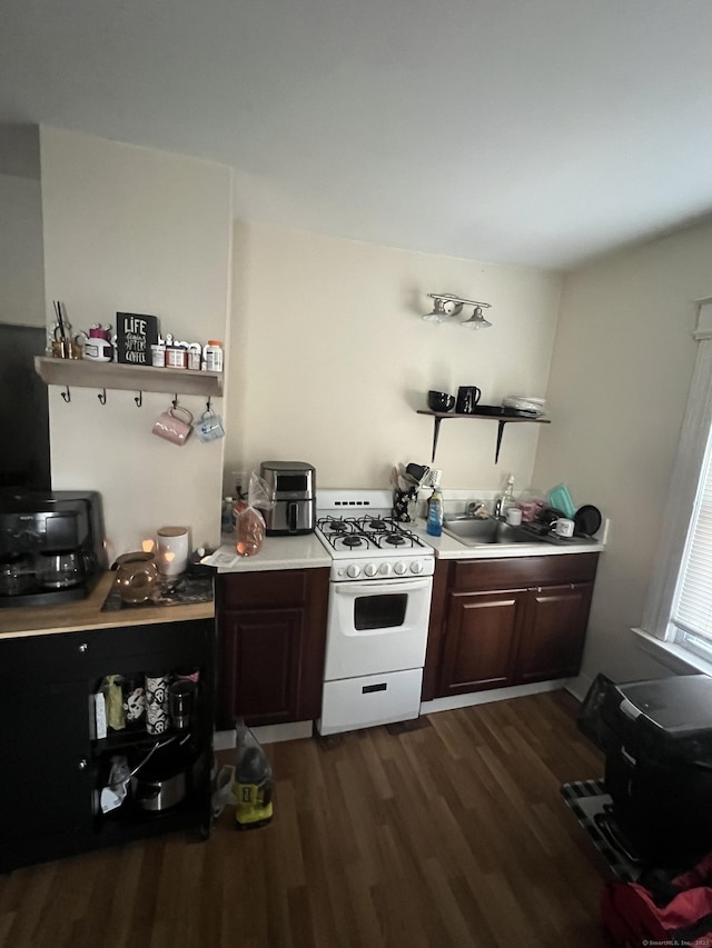 kitchen featuring white gas stove, dark wood-style flooring, a sink, light countertops, and open shelves